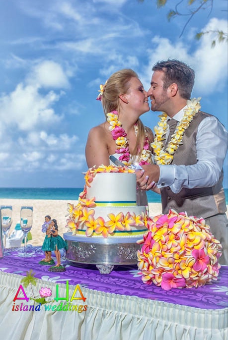 Chris cuts the cake with his bride as they give eachother Hawaiian kisses
